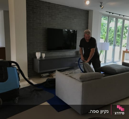 אדם מנקה ספה עם מכונת ניקוי מקצועית